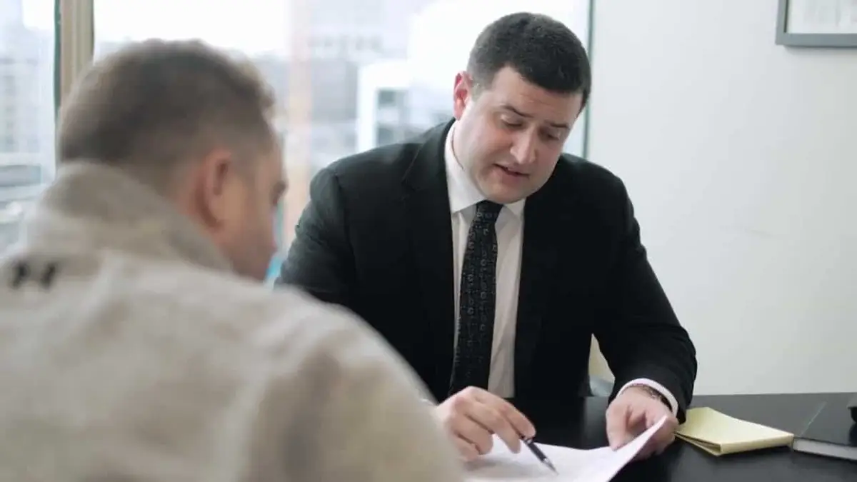 A lawyer in a dark suit reviewing papers at a desk with another person